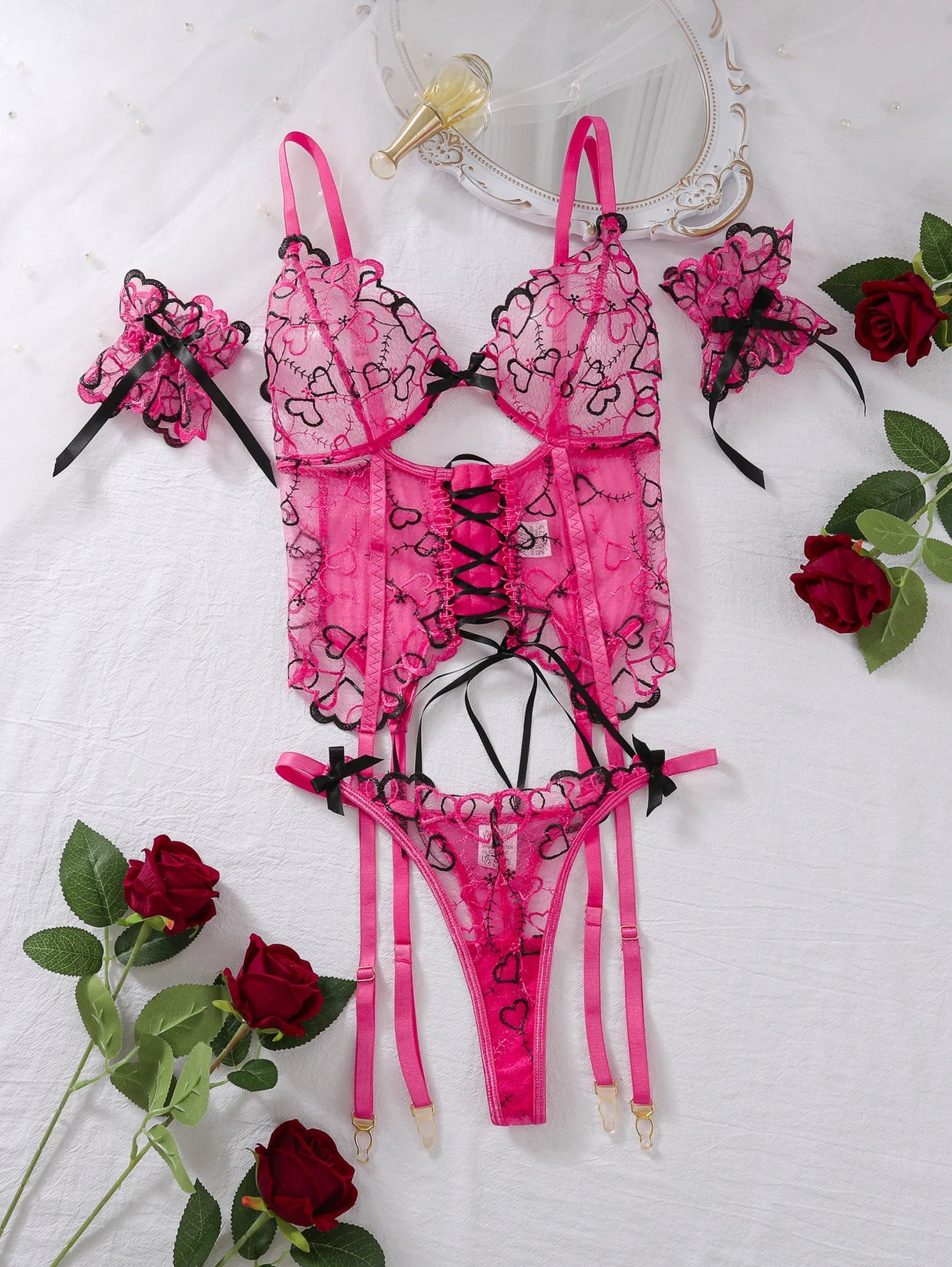 Flatlay of the black and pink lingerie set with lace hearts, ribbons and matching cuffs