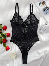 Flat lay of elegant black lace bodysuit with roses on white sheets